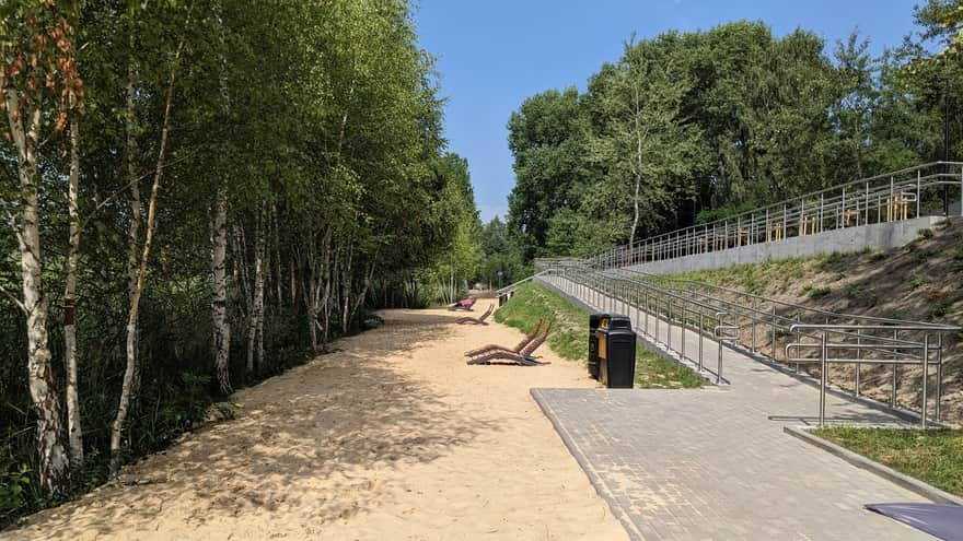 Część plaży z widokiem na drzewa, zjazd dla wózków i leżaki